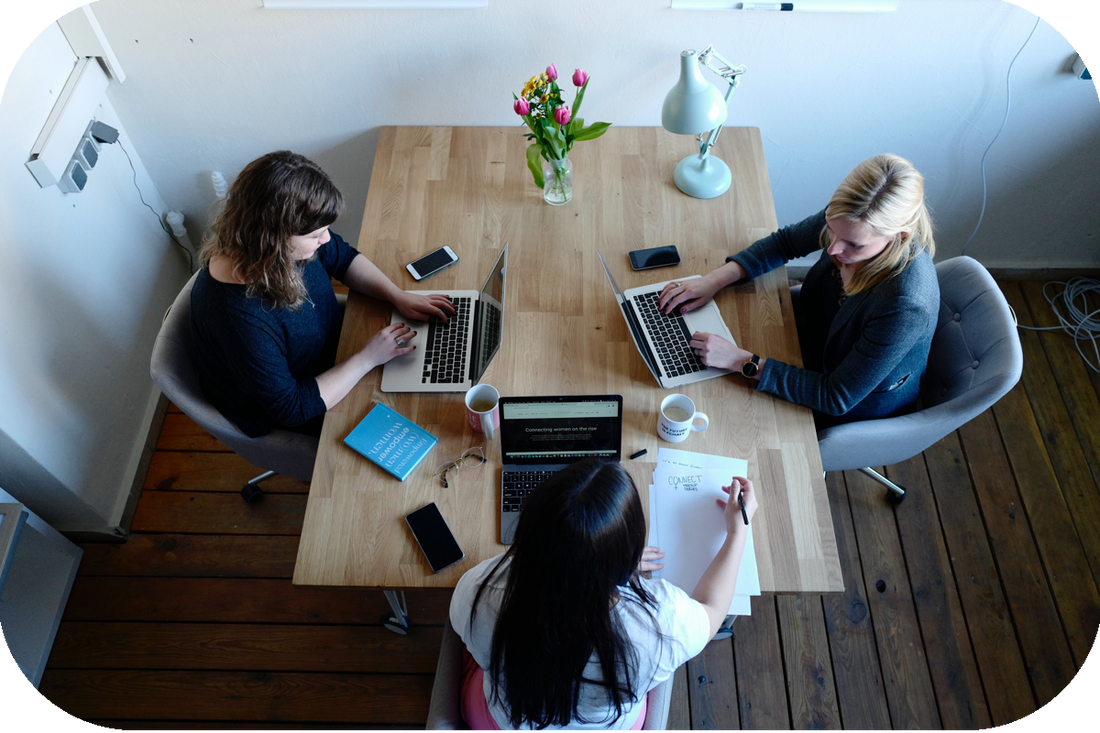 Group sit around a square table working on their laptops 